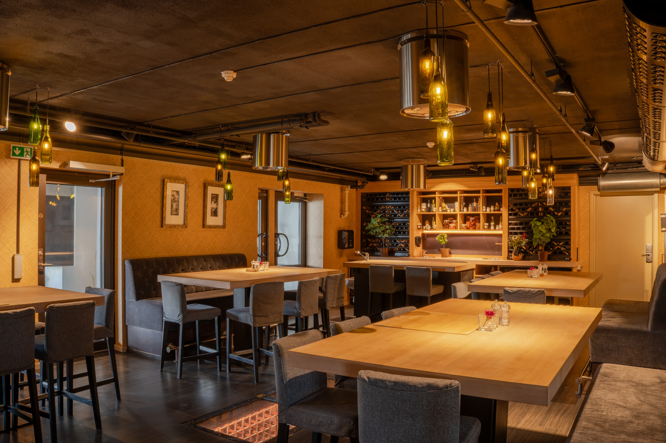 Bistroavdeling med vinflaskelamper i taket og vinlager i bakgrunnen