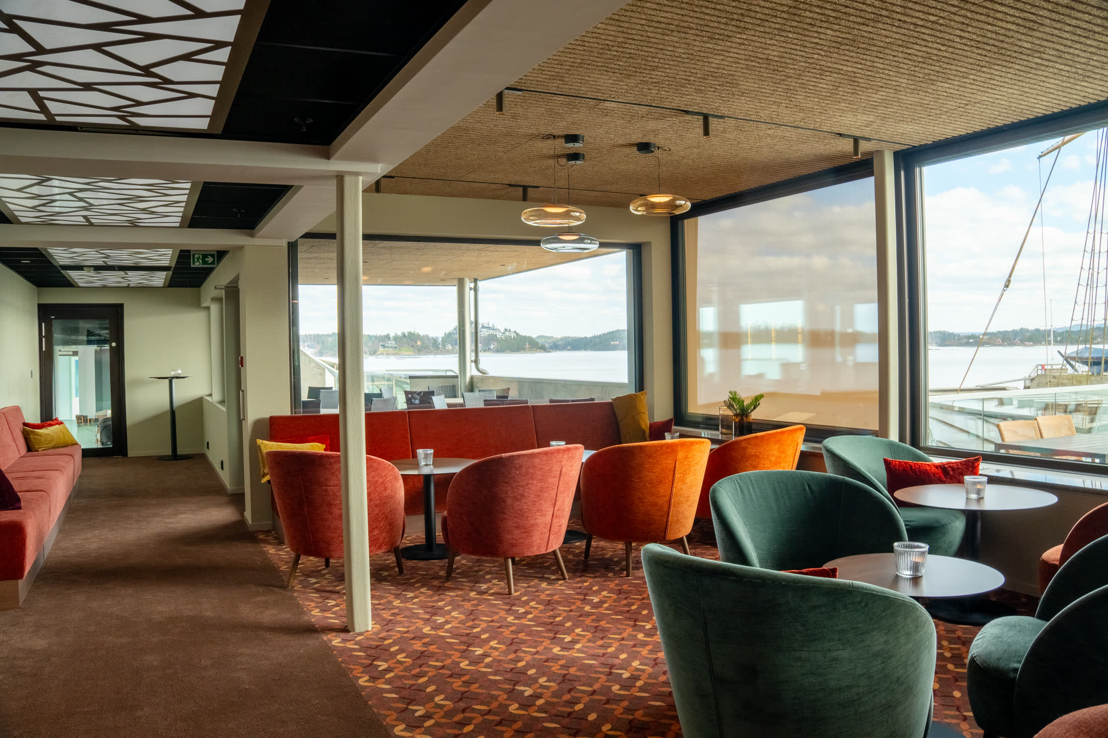Loungeområde med utsikt over fjorden og seilbåt gjennom vinduene